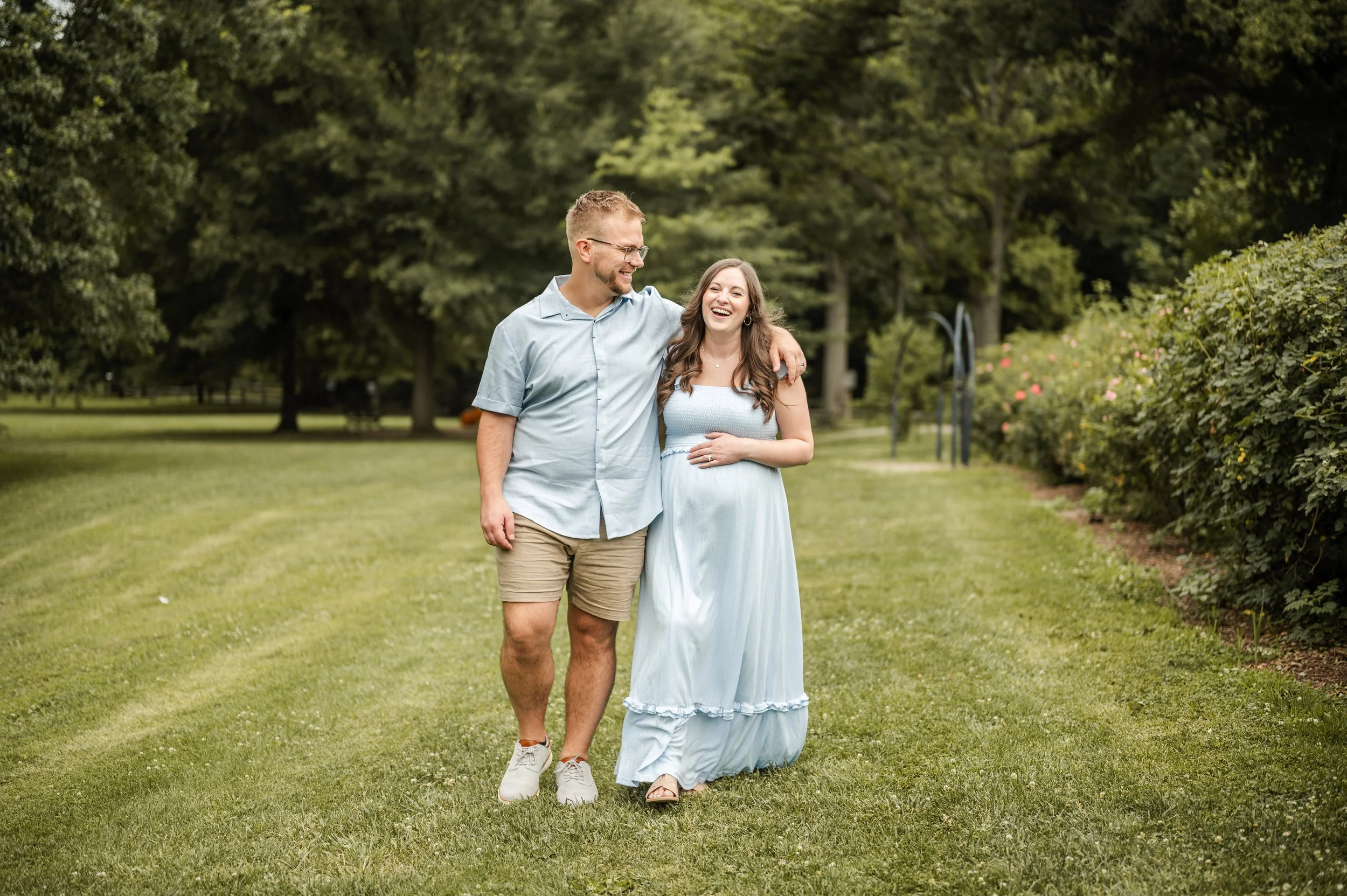 A smiling man and woman walking arm in arm in a park with green grass and trees, enjoying a sunny day bon air rose garden arlington virginia NOVA