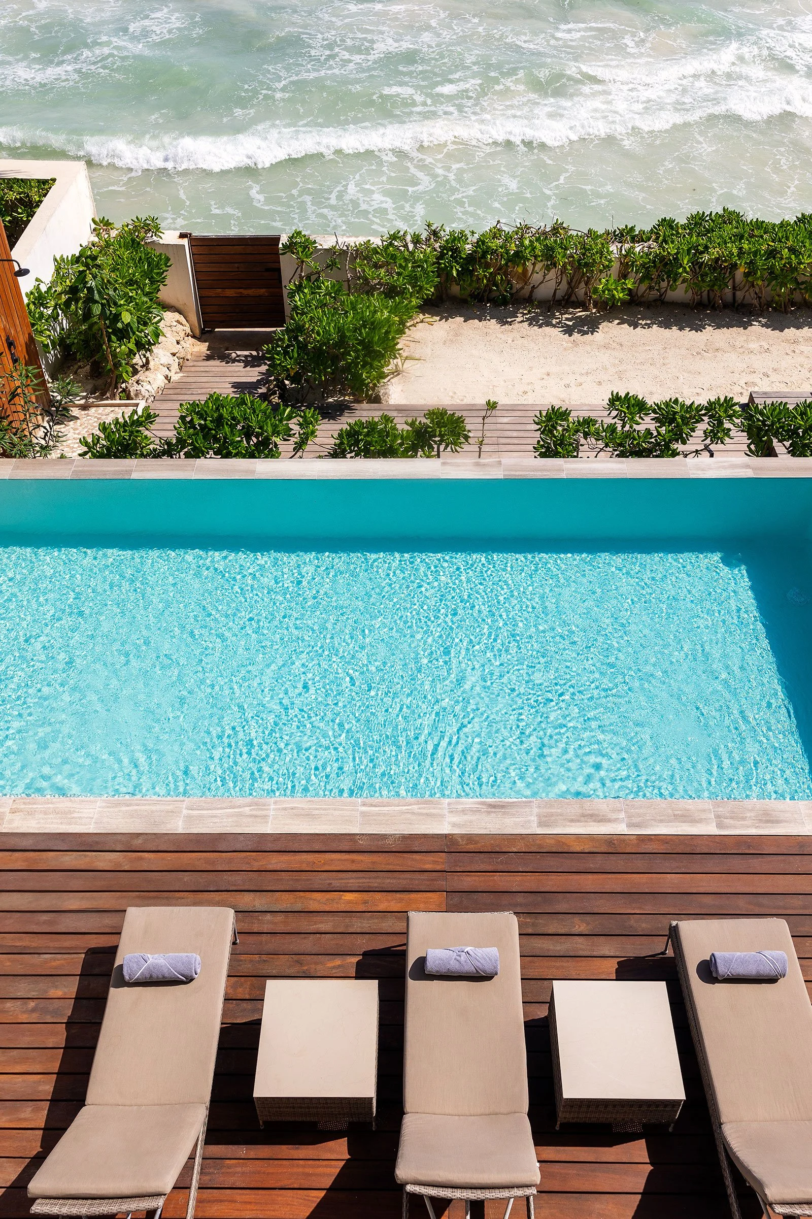 Poolside lounge chairs with towels facing a swimming pool and a view of the beach and ocean beyond.