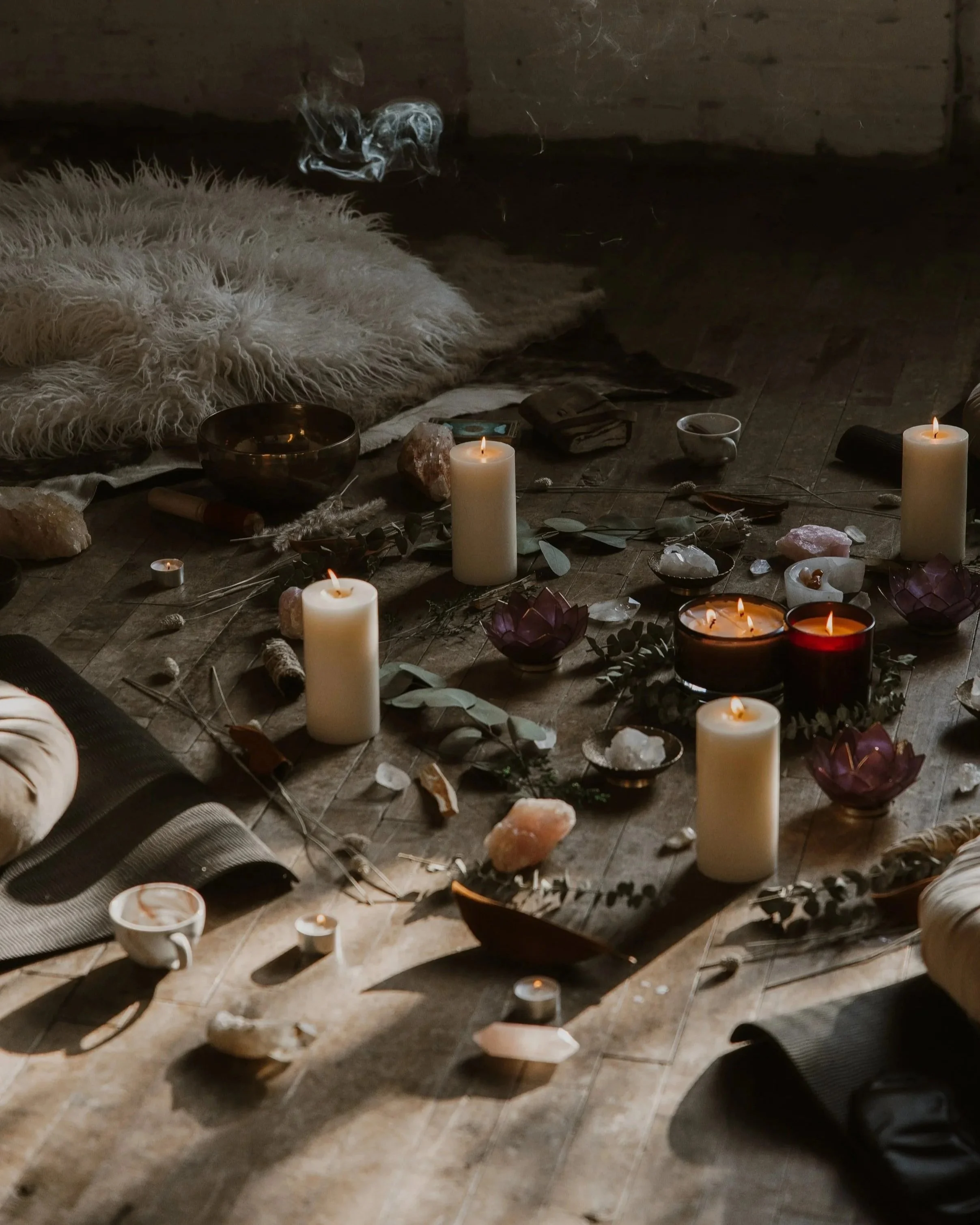 A cozy scene with candles, crystals, and decorative items on a wooden floor, featuring a fluffy rug, a bowl, and scattered objects.