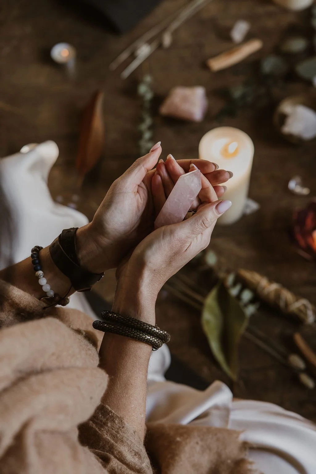 Person holding a pink crystal with various other crystals and stones on a wooden surface, lit by a candle.