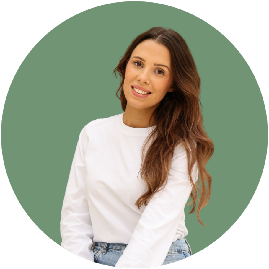 A smiling woman with long wavy brown hair wearing a white shirt and blue jeans against a green circular background.