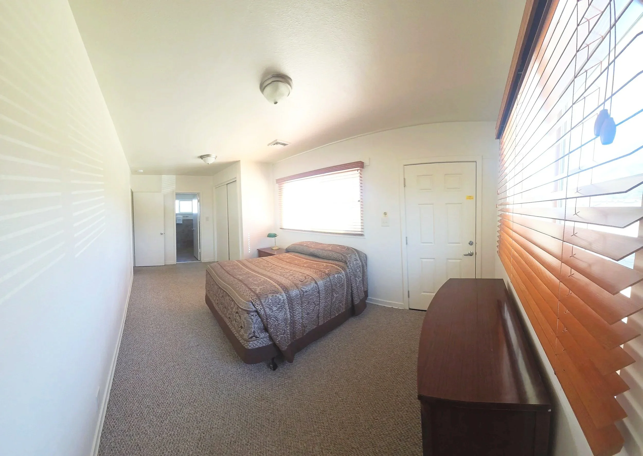 A bedroom with a bed, carpeted floor, and a window with wooden blinds