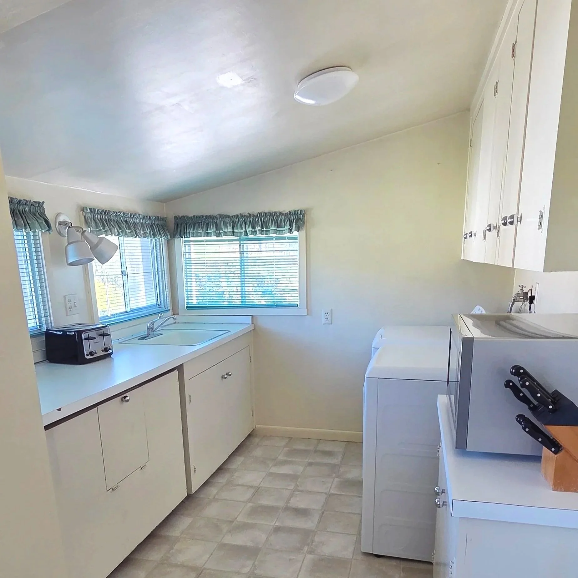 Small kitchen with white cabinets and appliances, a window with blue curtains, and a toaster on the counter.