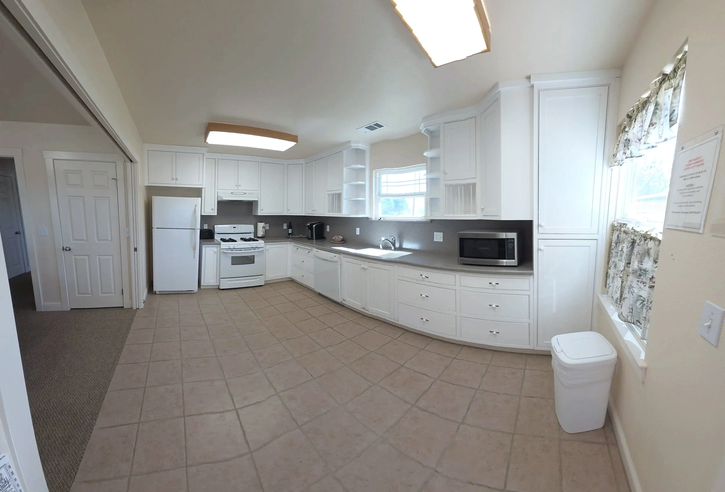 Kitchens with white cabinets, tile flooring, a refrigerator, stove, microwave, and small appliances, with windows having floral curtains.