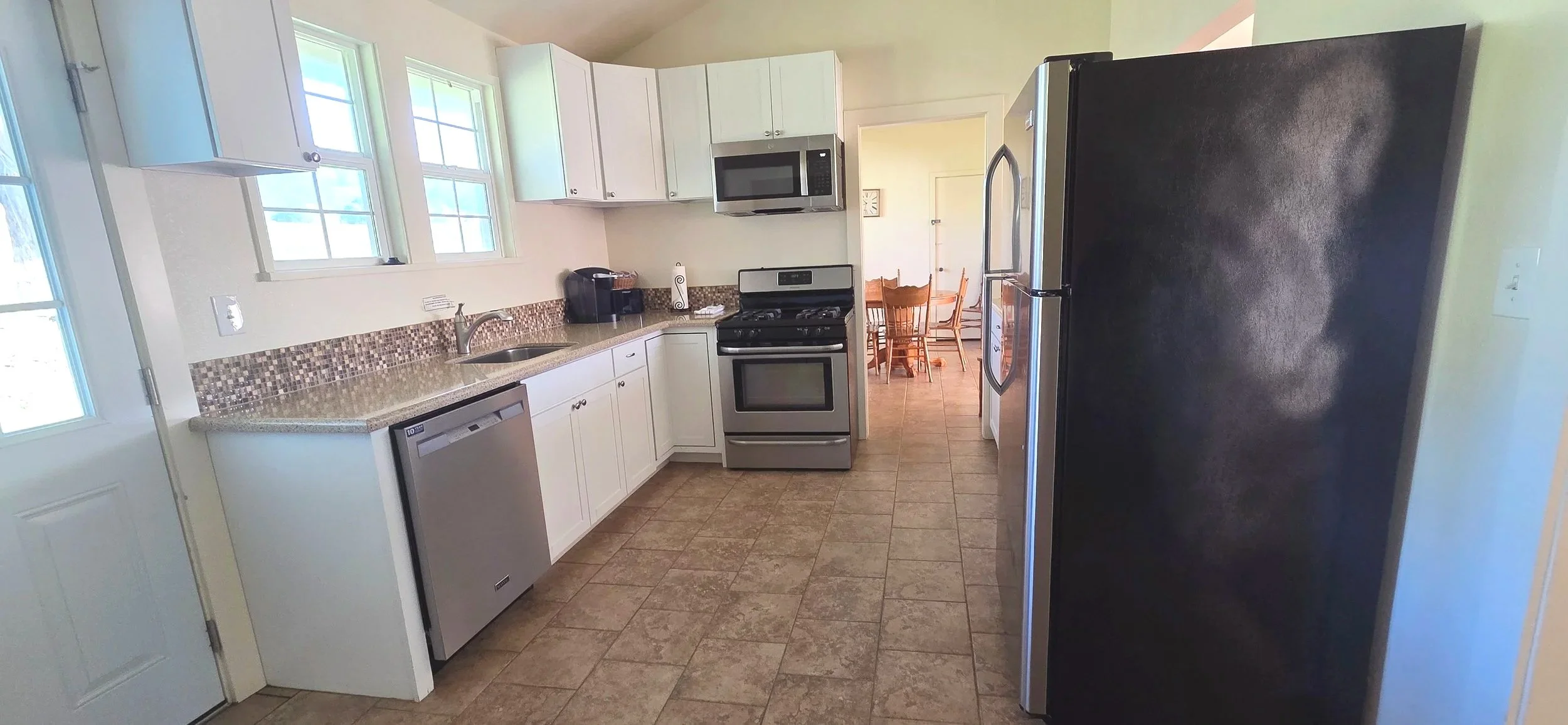 Kitchen with white cabinets, stainless steel appliances, a black refrigerator, a microwave, stove, dishwasher, and a small dining area in the background.