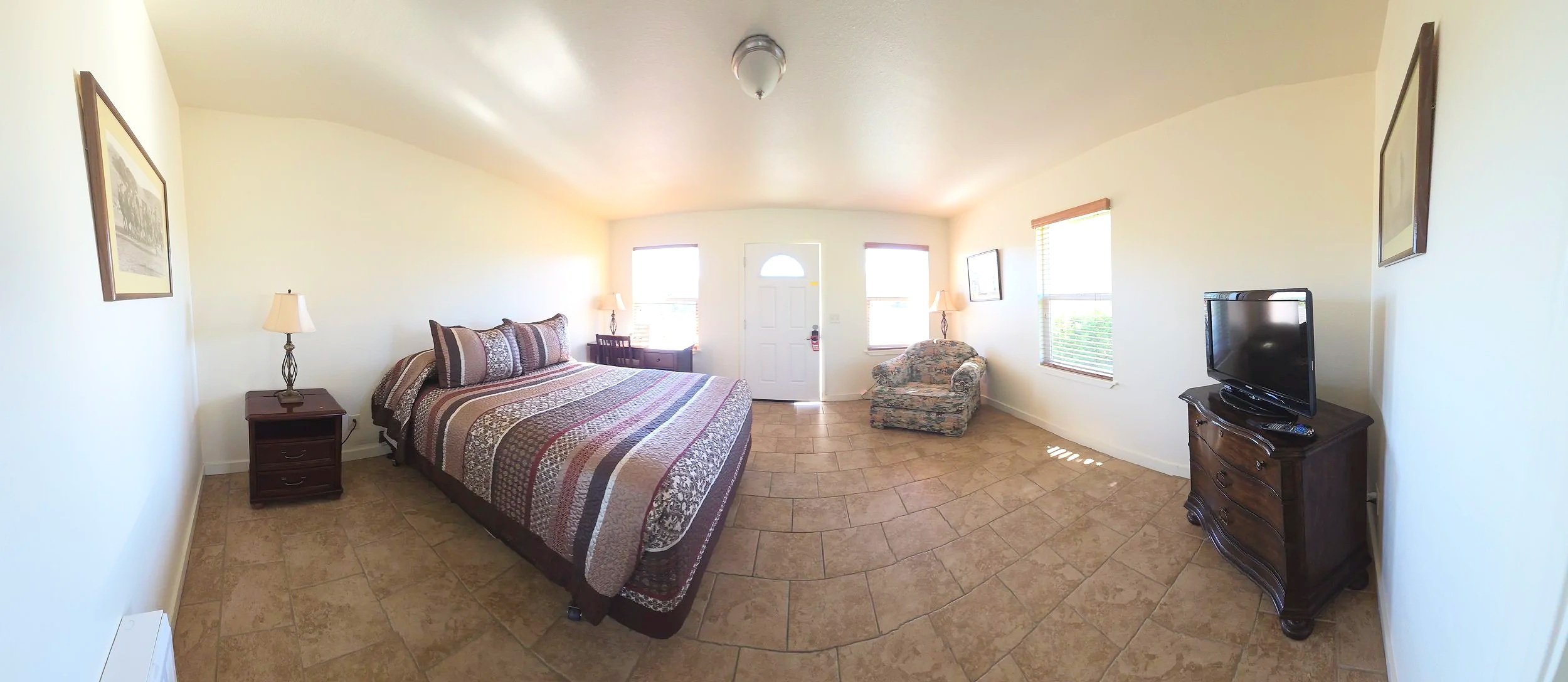 A hotel room with a bed, nightstands, lamps, an armchair, and a television.