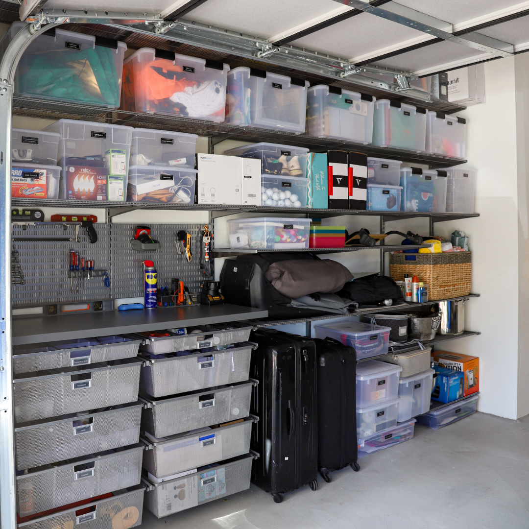 Organized garage with metal shelving holding storage bins, tools, and luggage.
