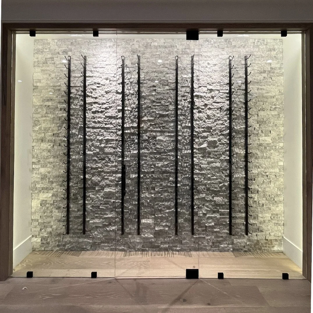 Modern glass display case with a gray stone wall background and black metal hooks arranged in rows.