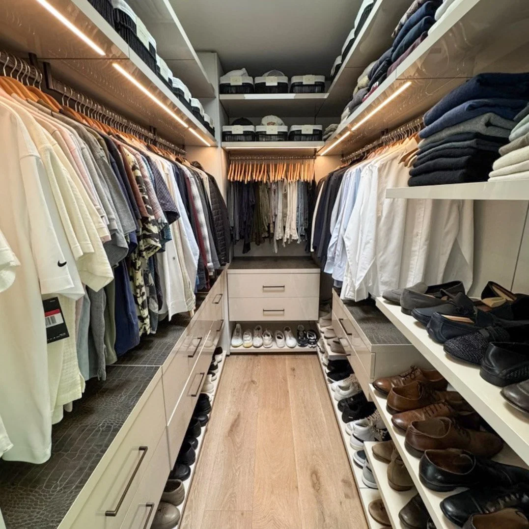 A walk-in closet with clothes hanging on both sides, shoes on shelves below, and boxes on the ceiling shelves.