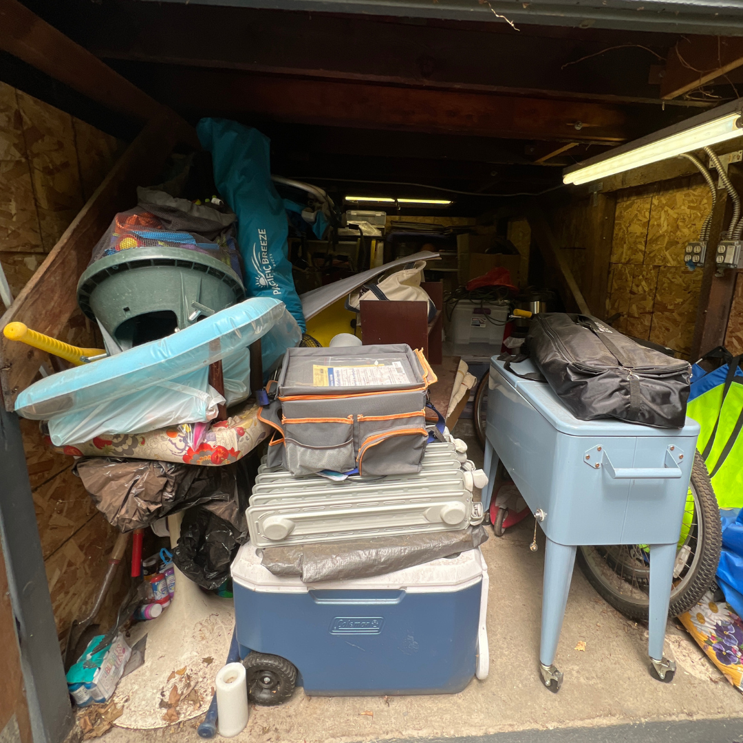 Cluttered garage storage with cooler, toolbox, luggage, bicycle, and various household items.