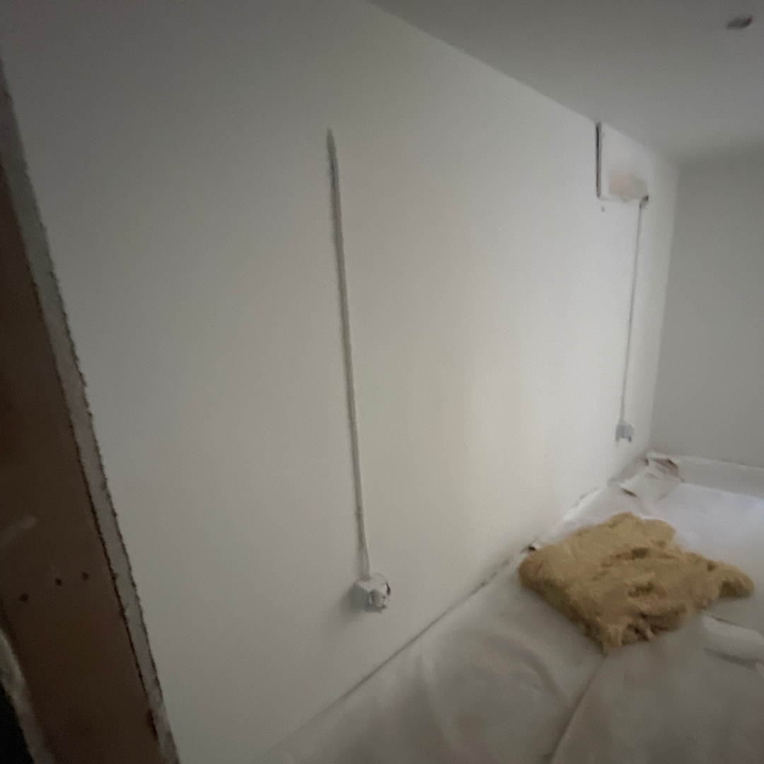 A room under construction with exposed electrical wiring, insulation on the floor, and drywall panels partially installed.