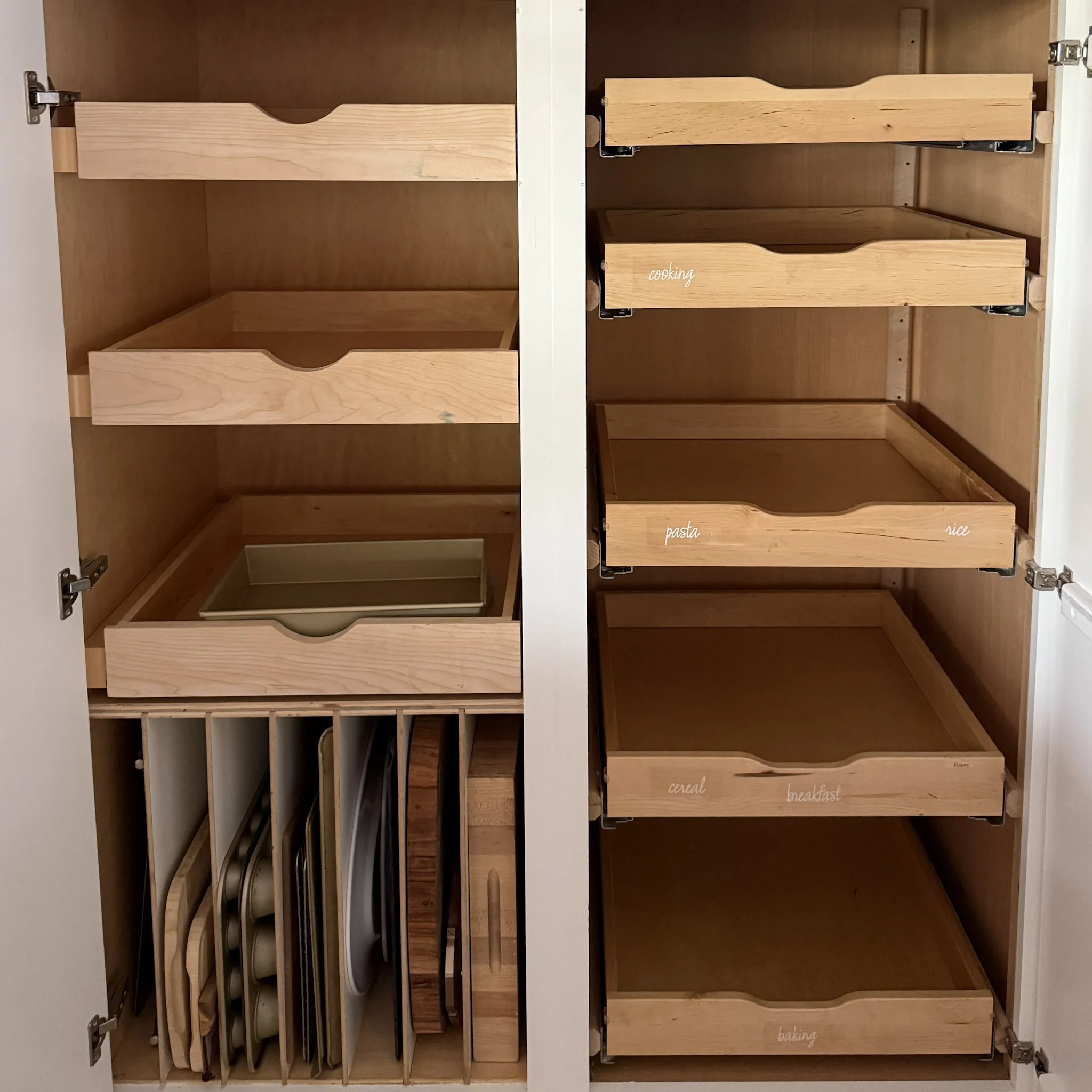 Open kitchen cabinet with labeled wooden pull-out drawers, including labels for 'cereal', 'breakfast', 'pasta', and 'rice'.