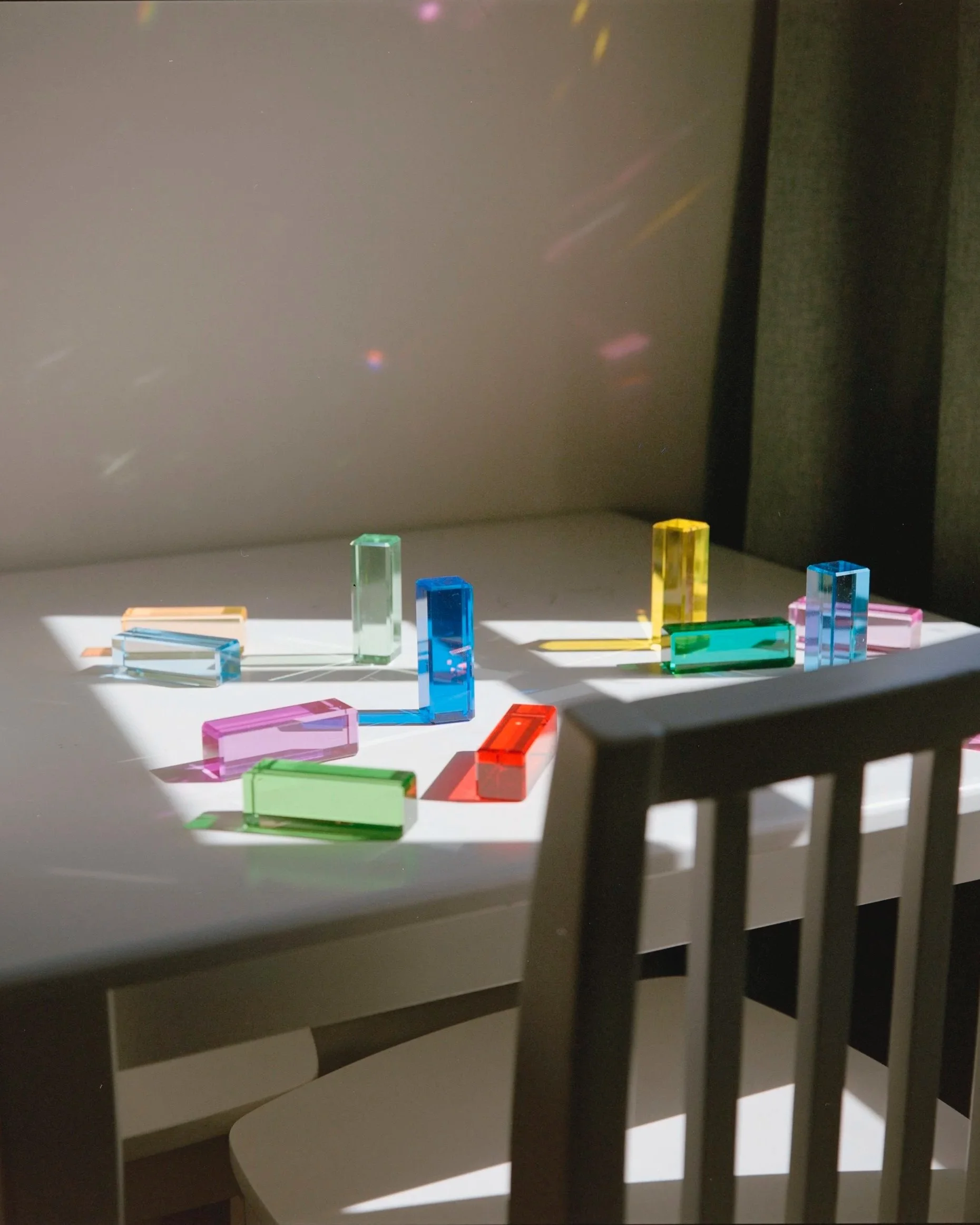 Colorful acrylic rectangular blocks arranged on a white surface, with shadows cast by nearby blinds or a window.
