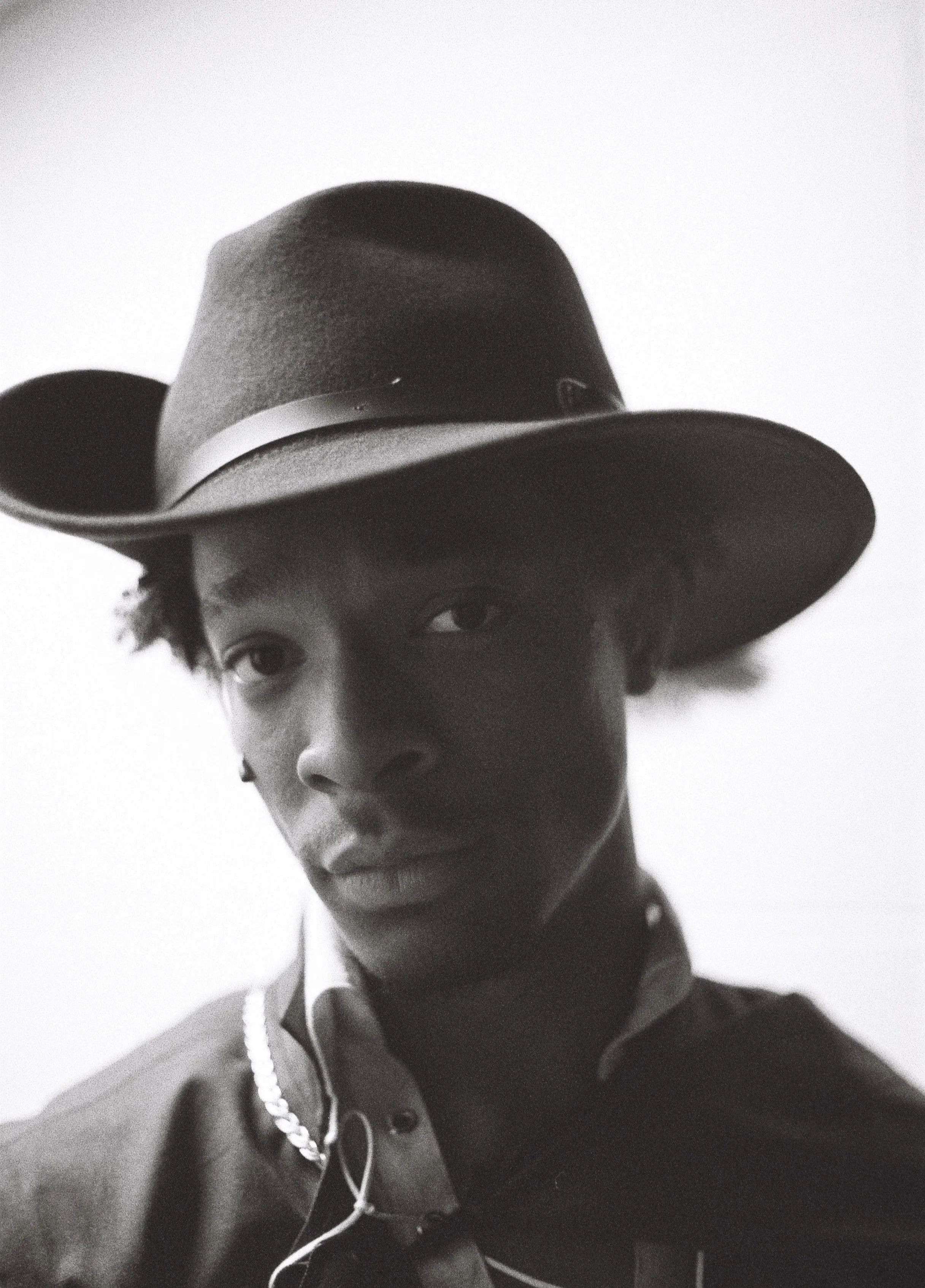 Black and white photo of a Cardinal Captain wearing a wide-brimmed hat, collared shirt, and a chain necklace, looking directly at the camera with a neutral expression.