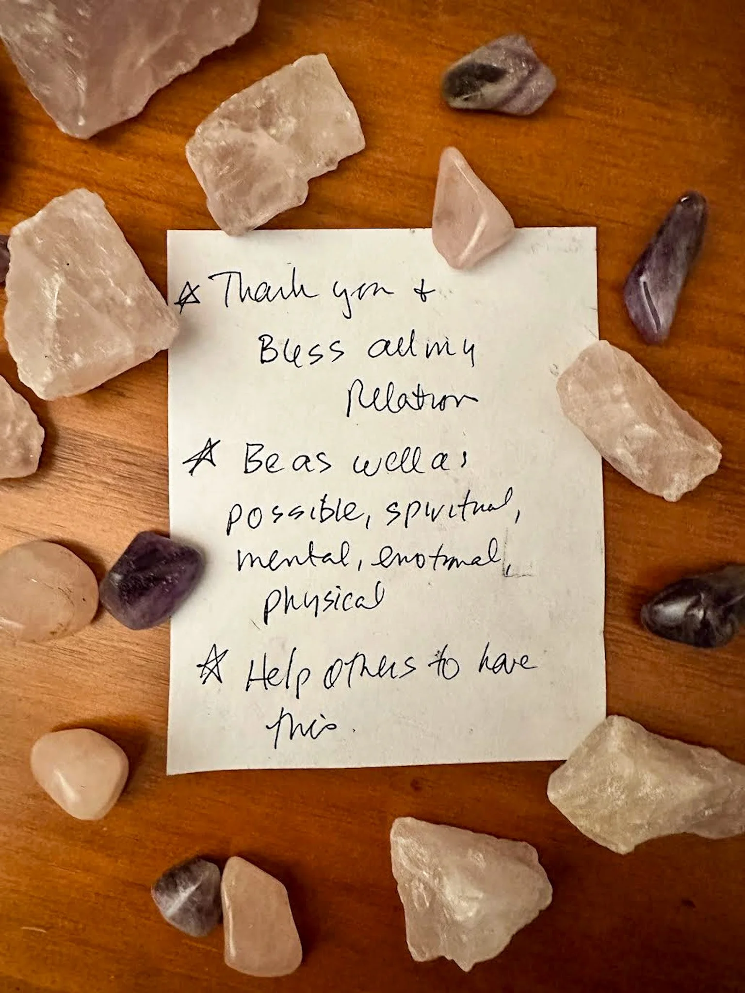 A photo of a note Lauren's mentor Wanda wrote before she died. It's surrounded by crystals. It reads: Thank you and bless all my relations. Be as well as possible, spiritual, mental, emotional, physical. Help others to have this.