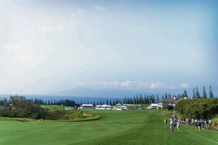 A golf course overlooking the ocean with people walking and a golf cart in the distance.