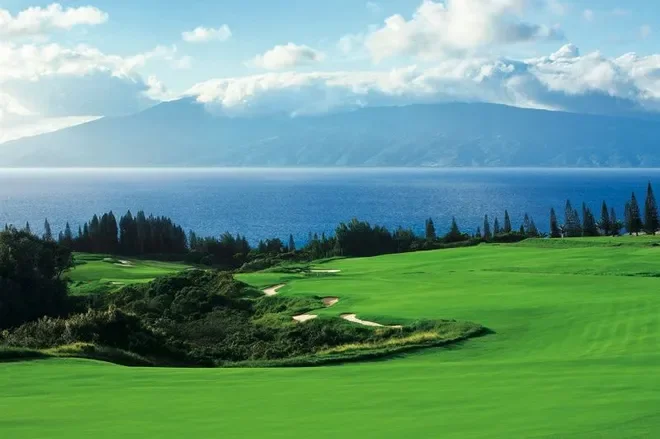 A scenic golf course next to a large body of water with mountains in the background.