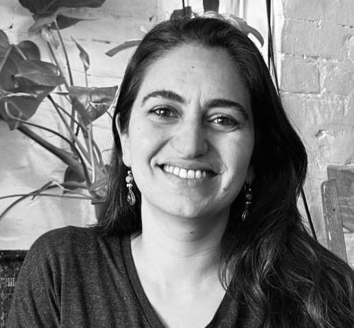 Black and white photo of a smiling woman with shoulder-length dark hair, wearing glasses on her head and a sleeveless top.