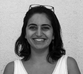 Black and white photo of a woman with shoulder-length hair, wearing a sleeveless top and glasses on her head, smiling.