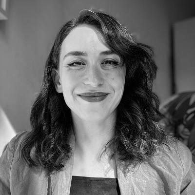 A woman with wavy hair smiling at the camera in a grayscale photo.
