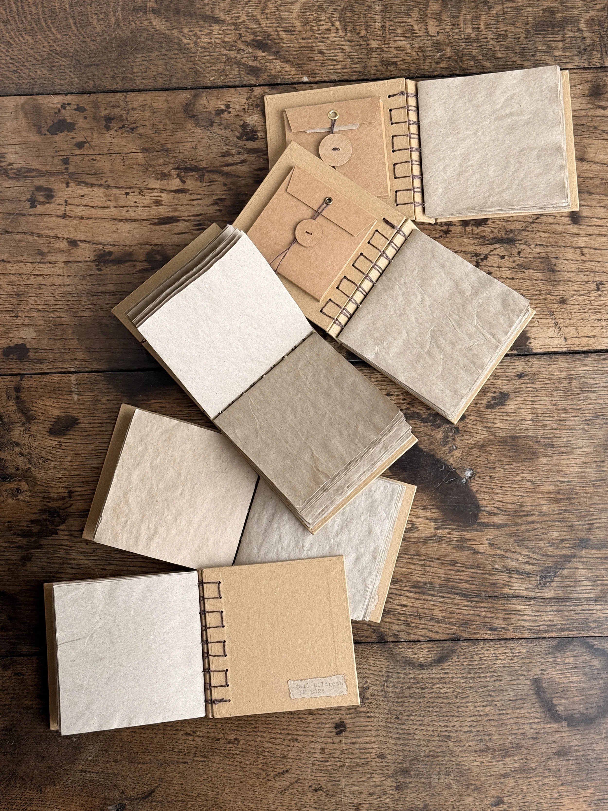 Multiple small spiral-bound notebooks with blank pages and brown envelopes on a wooden surface.