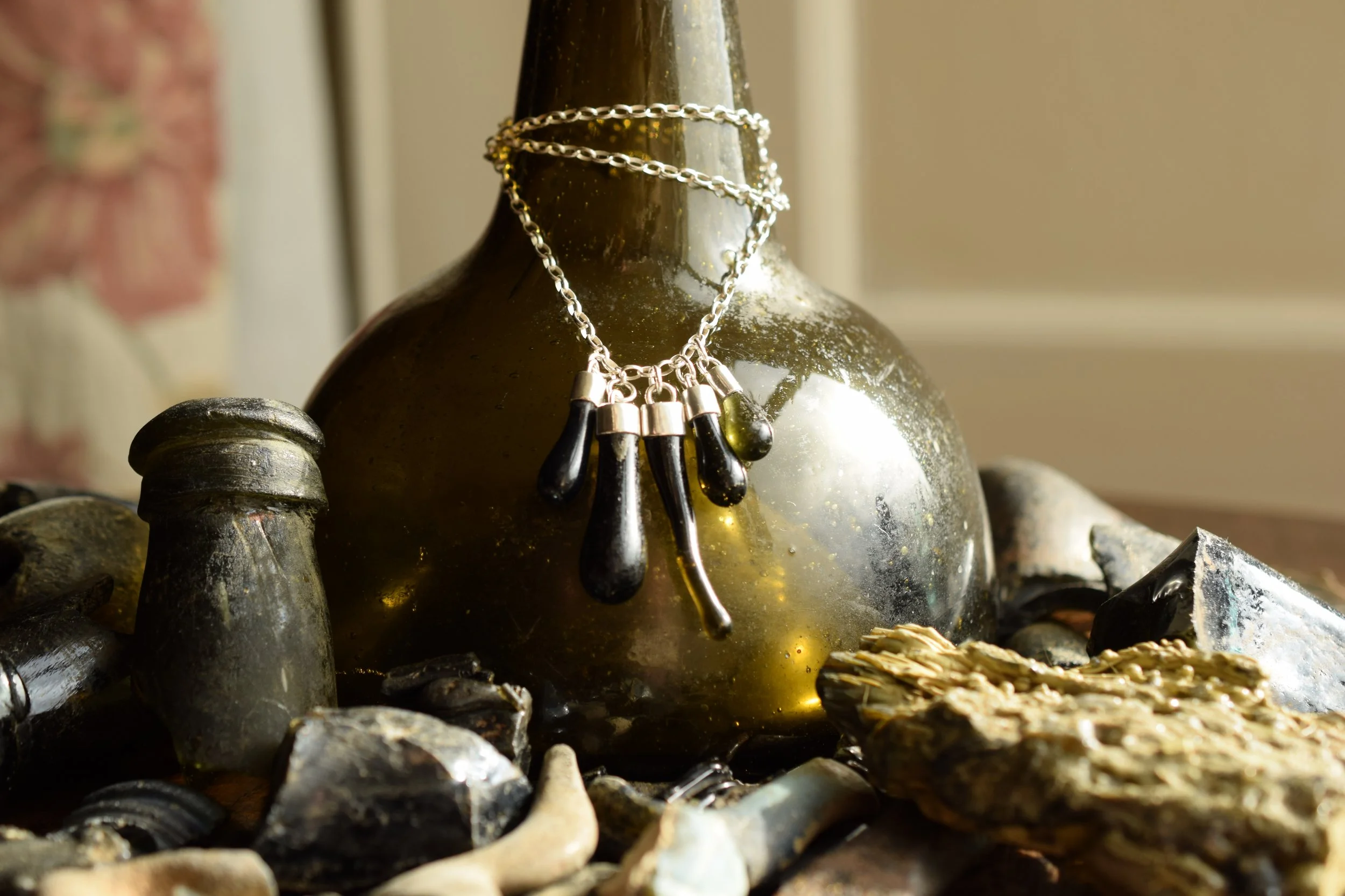 A vintage glass bottle with jewelry on top, surrounded by rocks and minerals.