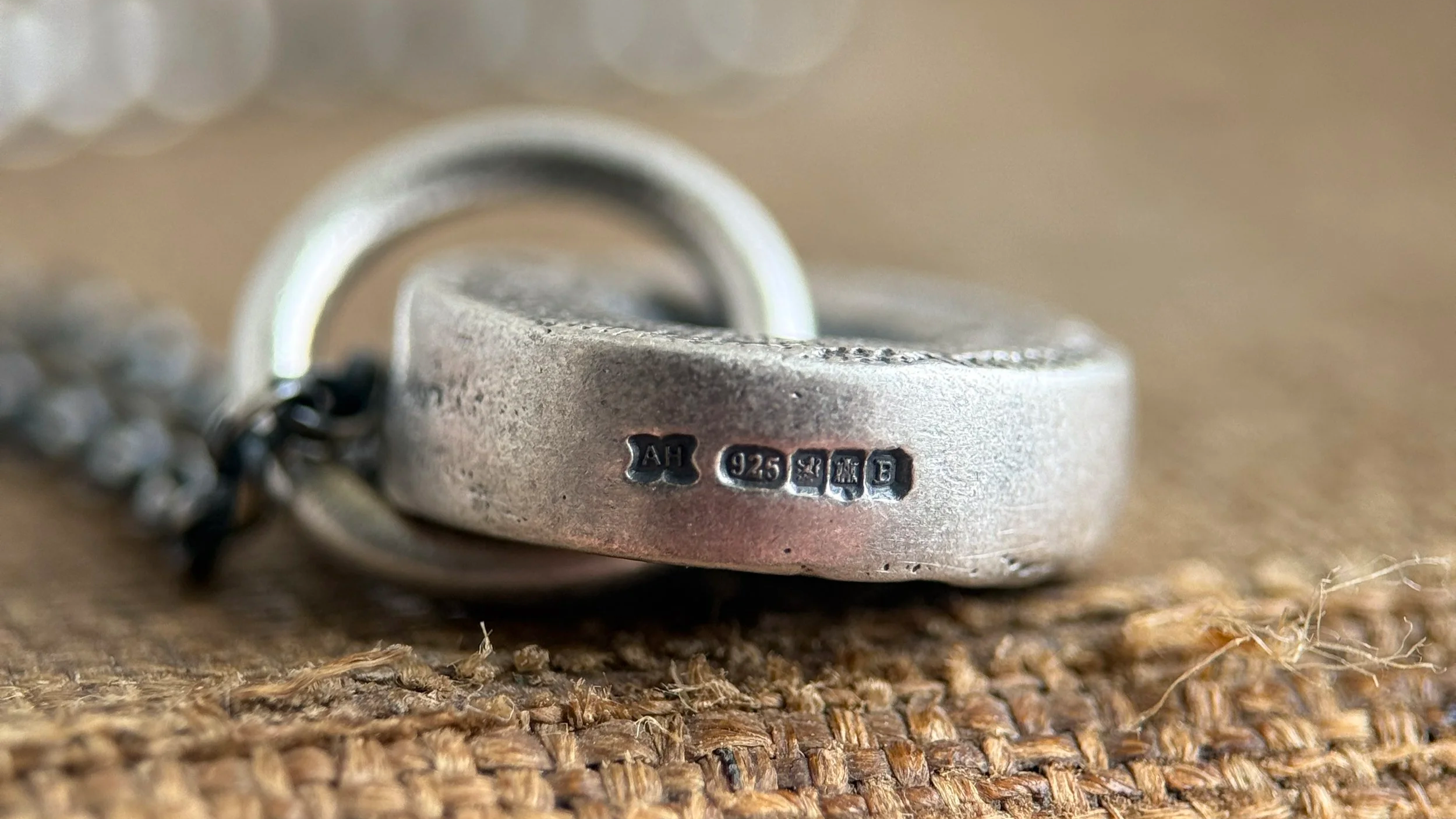 Close-up of a silver ring with hallmarks and a chain on a textured wooden surface.