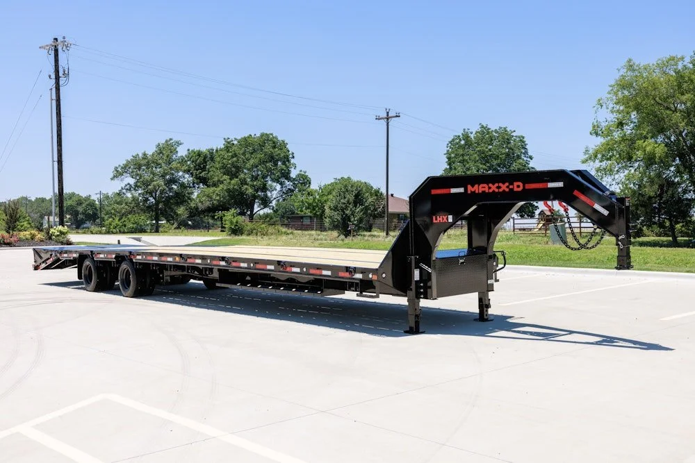 Black flatbed trailer parked in a parking lot with trees and utility poles in the background.