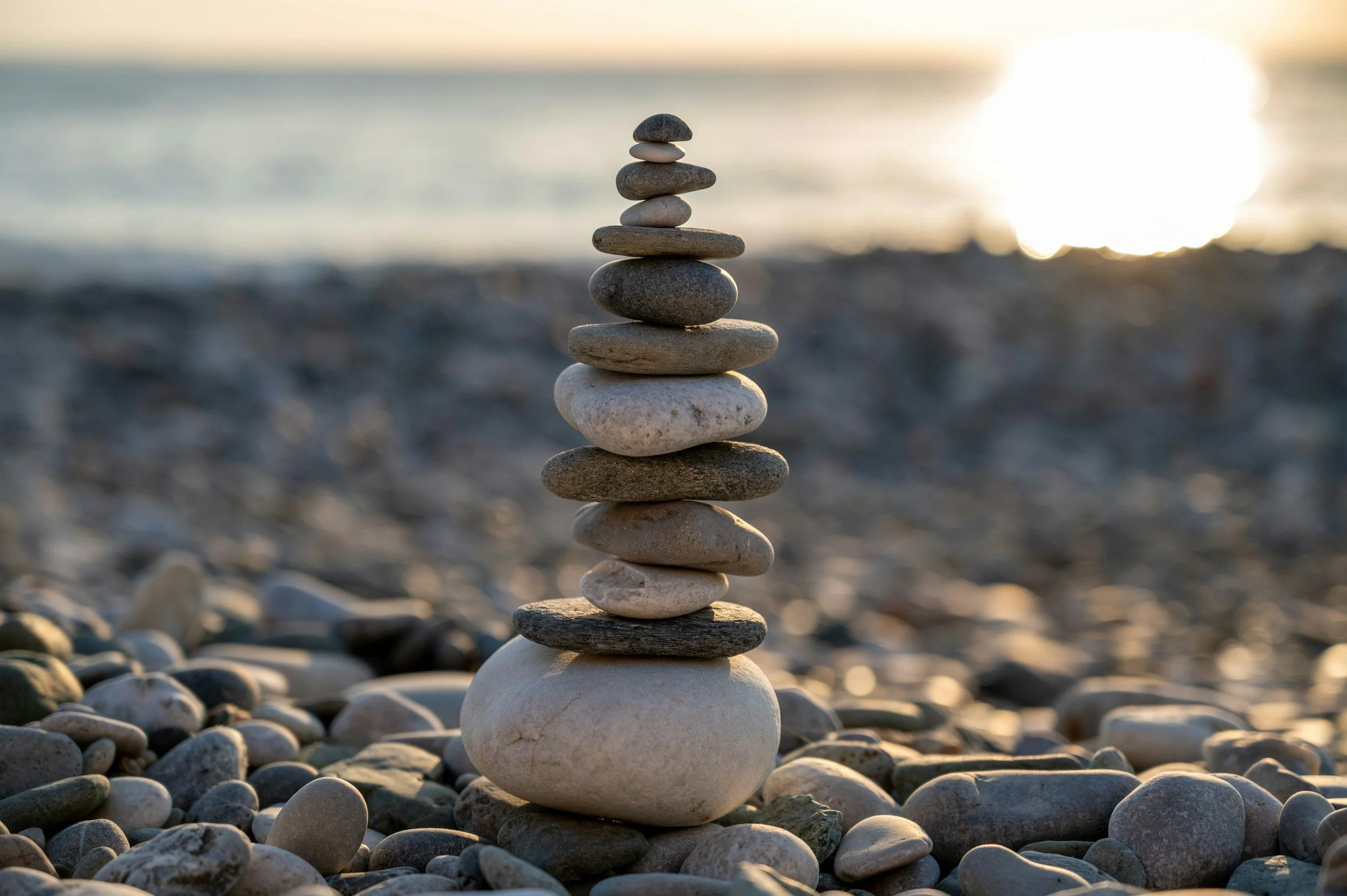 Stacked balanced stones on pebble beach near the water at sunset