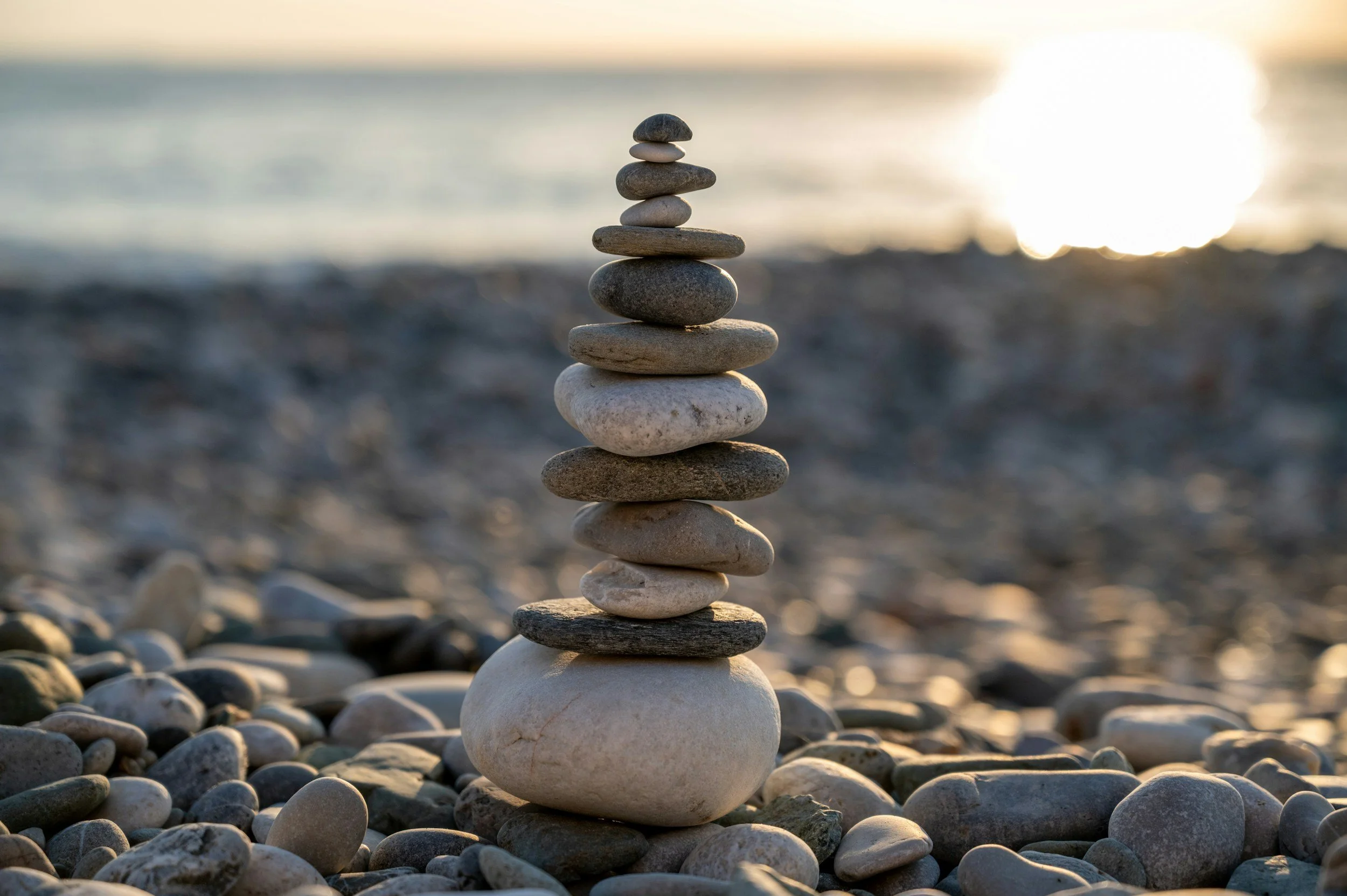 Stacked rocks symbolizing stability, resilience, and mental wellness with warm sunlight behind them.