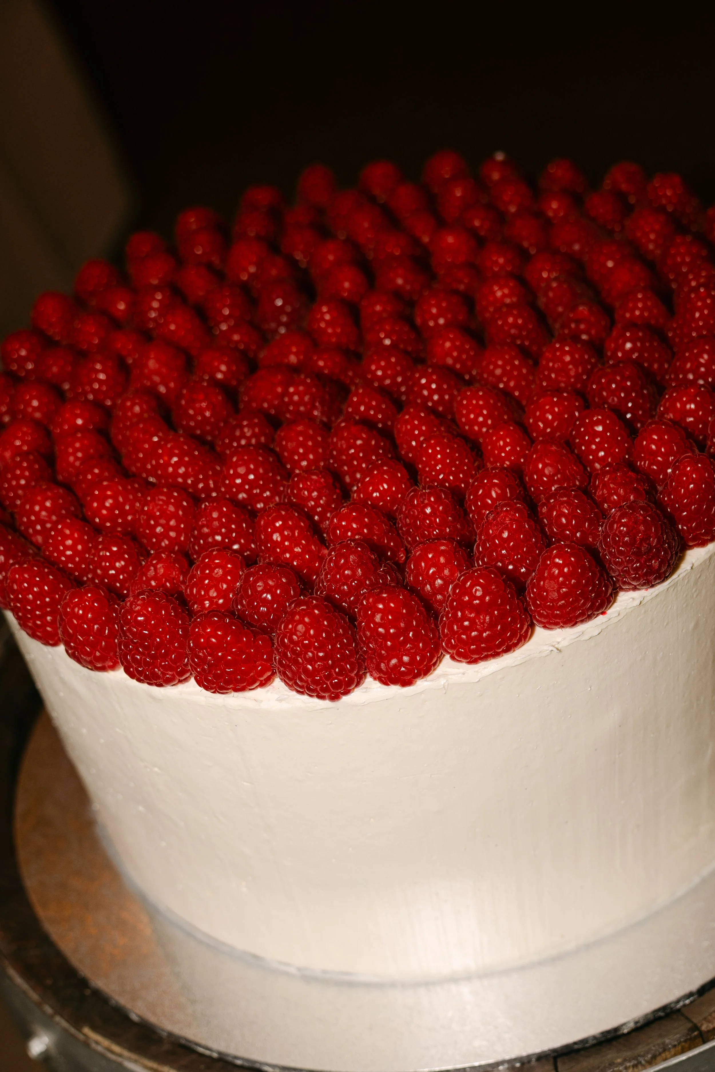 A round cake with white frosting topped with a large number of fresh red raspberries