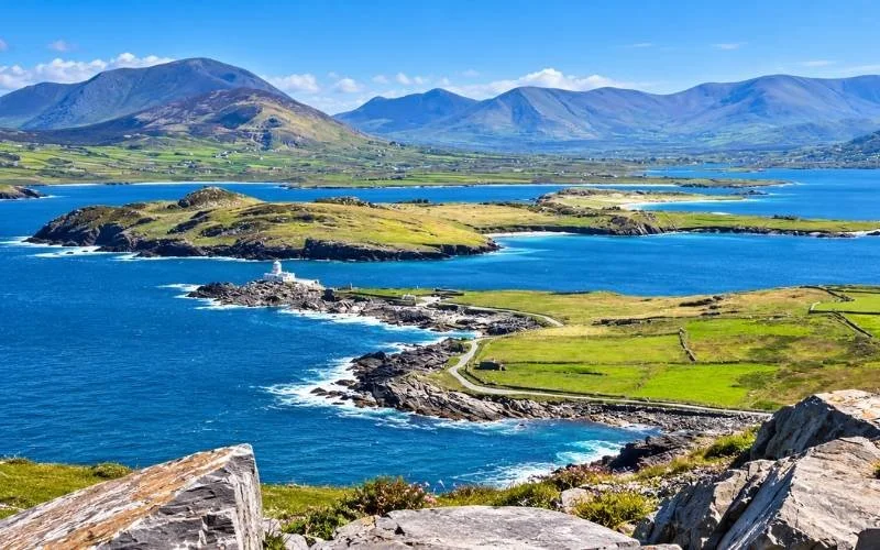 Panoramic view of the Skellig Ring coastline in County Kerry, featuring turquoise Atlantic waters, green fields, rocky headlands and distant mountains.