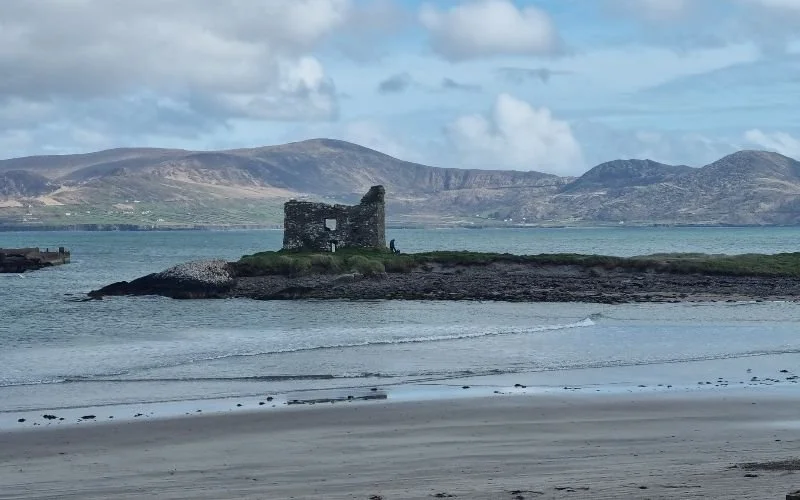 Historic stone tower overlooking a sandy beach and Atlantic coastline along the Skellig Coast in County Kerry.