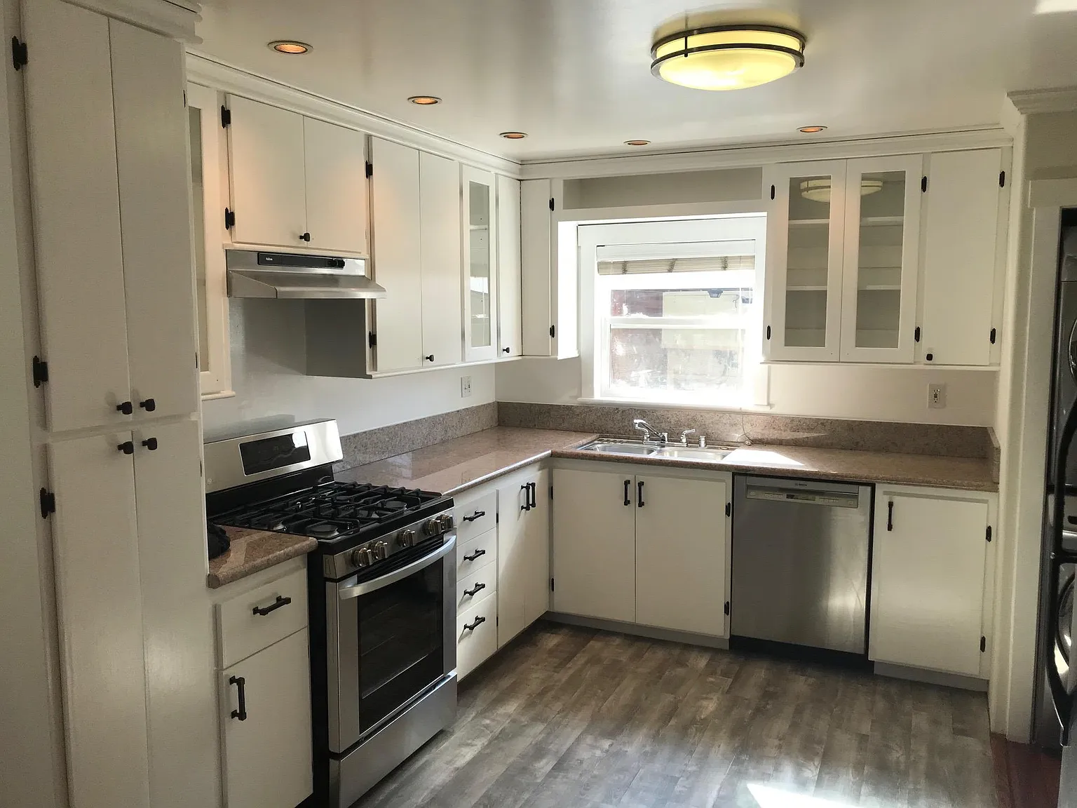 Kitchen with white cabinets, a window above the sink, stainless steel appliances, granite countertops, and wood-style flooring.