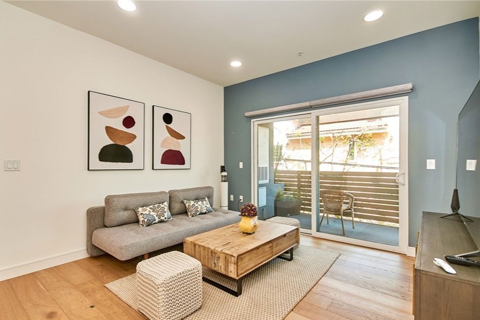 Living room with grey sofa, wooden coffee table, abstract wall art, sliding glass door opening to patio, and wooden flooring.