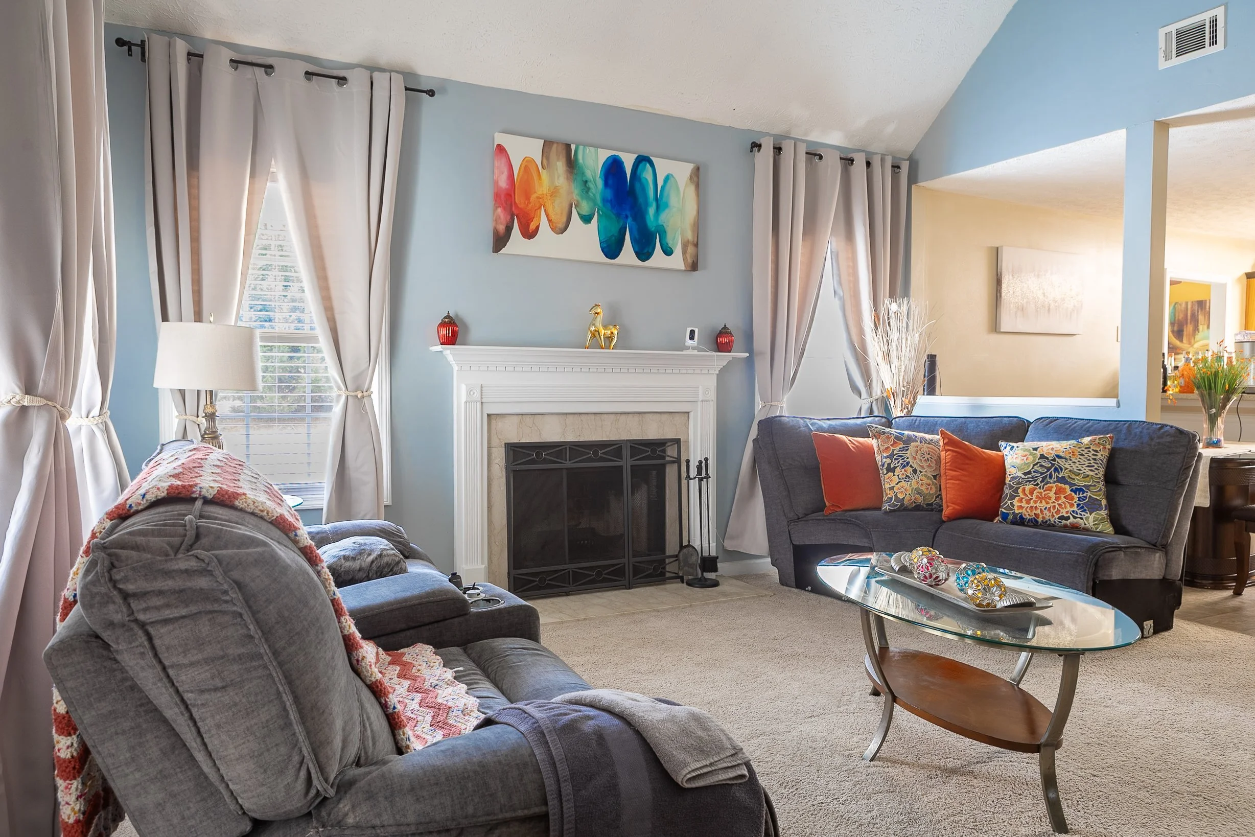 Living room with gray and blue couches, a fireplace, and various colorful pillows and decorations.