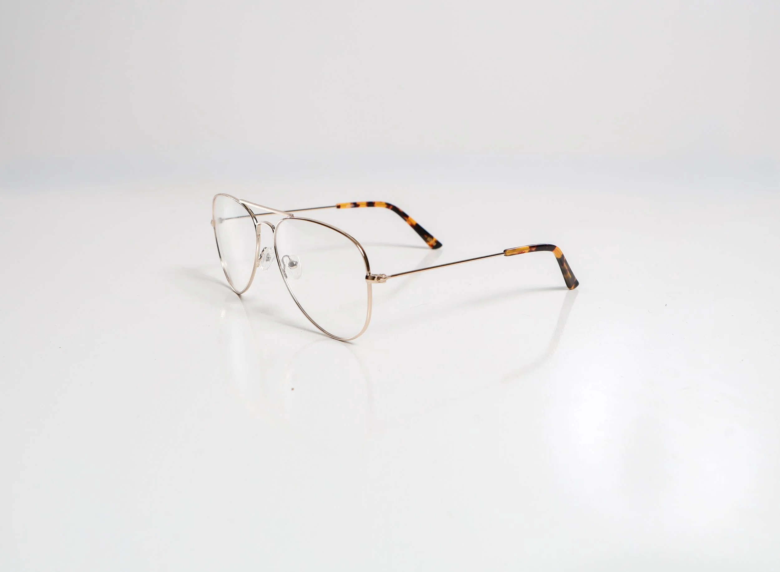 Gold-colored eyeglasses with tortoise-shell patterned arms resting on a white surface.