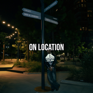 Person standing near street sign at night in a park with string lights and trees.