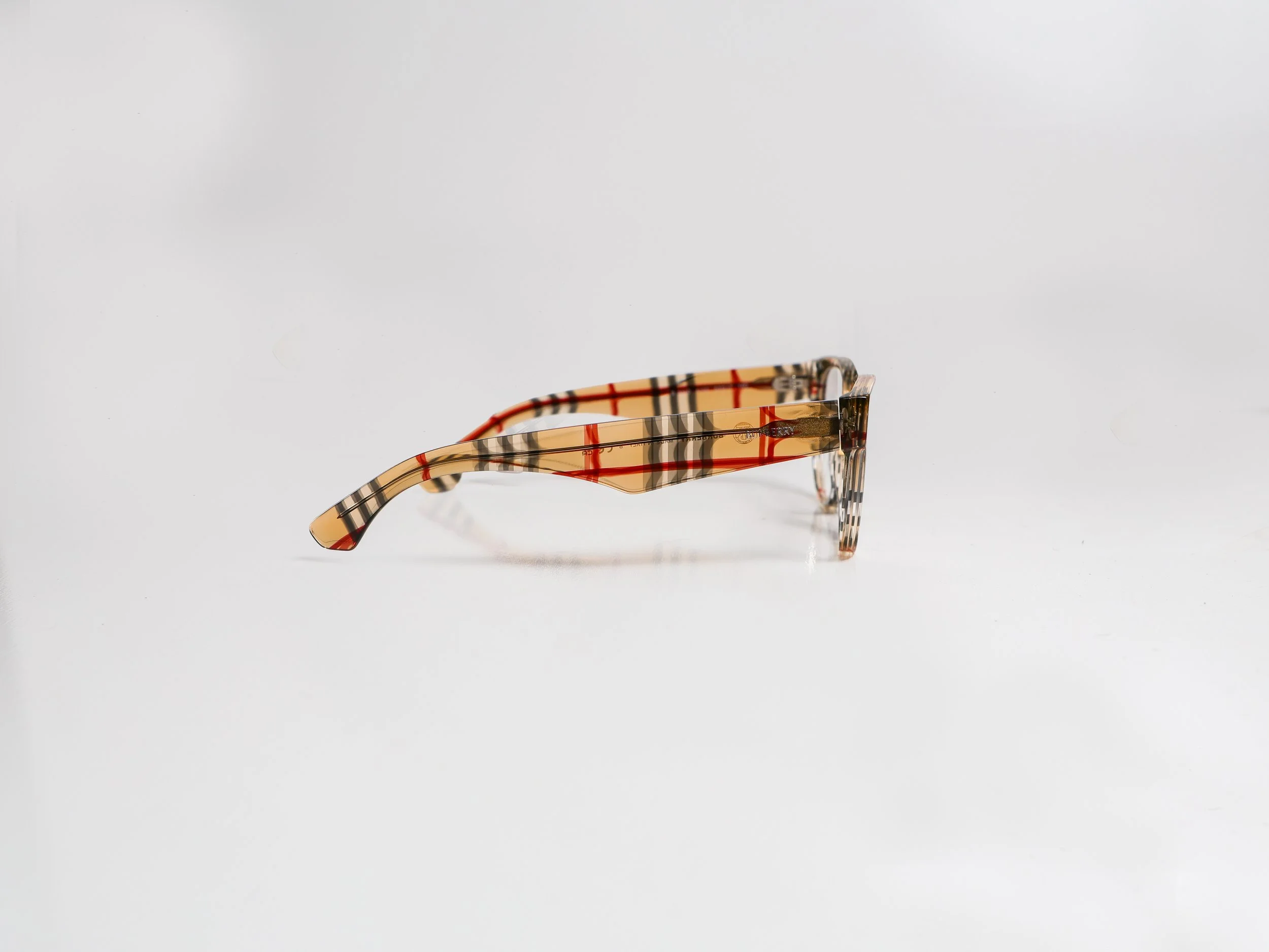 Tortoiseshell-patterned eyeglasses with brown, red, and black stripes, resting on a plain white surface.