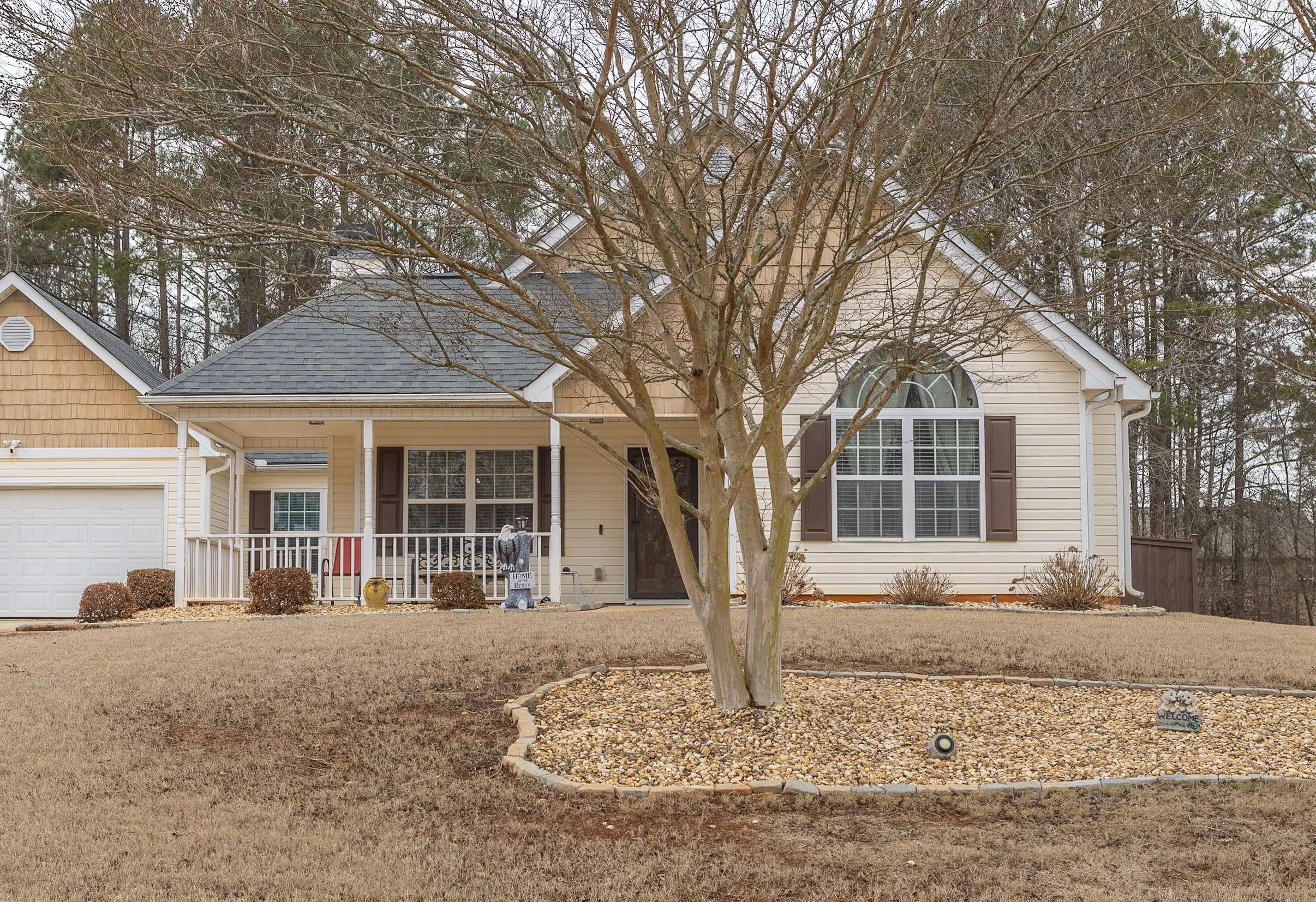 Front view of a house with a tree in the front yard and a landscaped circular area with gravel.
