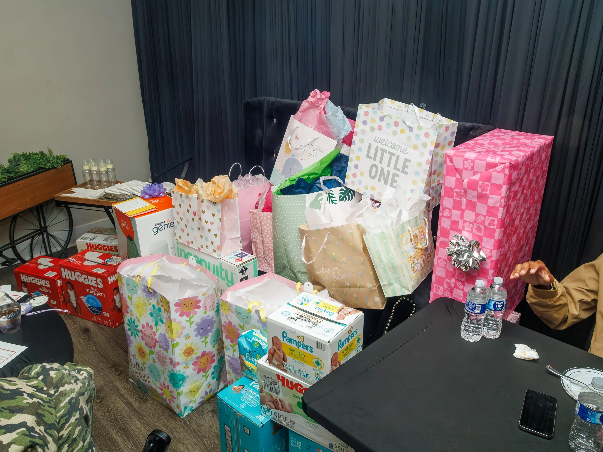 Gift bags and boxes arranged on a table, with some water bottles and a hand visible on the right side.