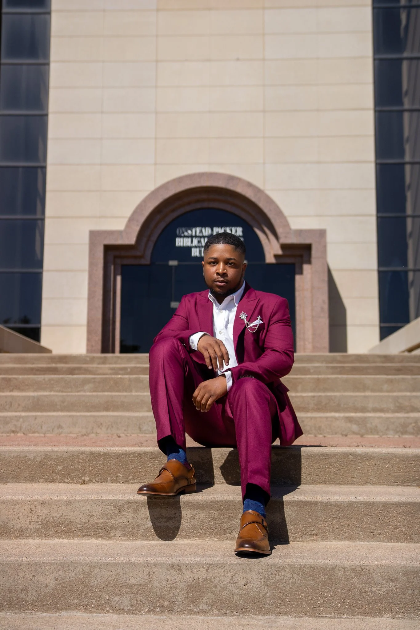 A man in a maroon suit sitting on steps in front of a building with a sign that reads 'Ostend Bicker Black Bock'.