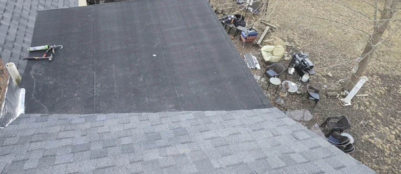 Aerial view of a backyard with a house roof, patio furniture, a barbecue grill, trees, and other outdoor items.