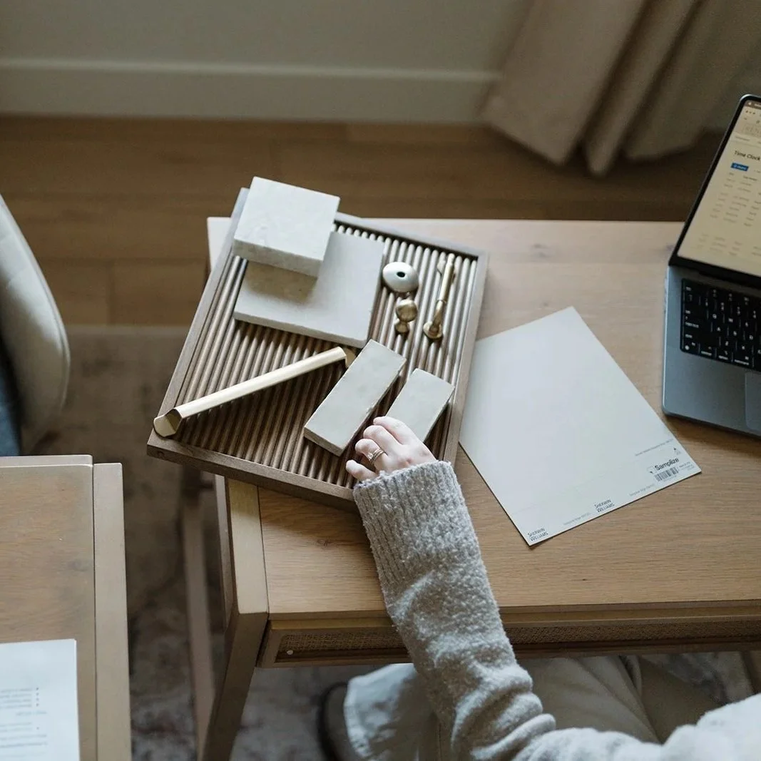 Interior designer arranging wooden blocks and objects on a tabletop, with a laptop and papers nearby.