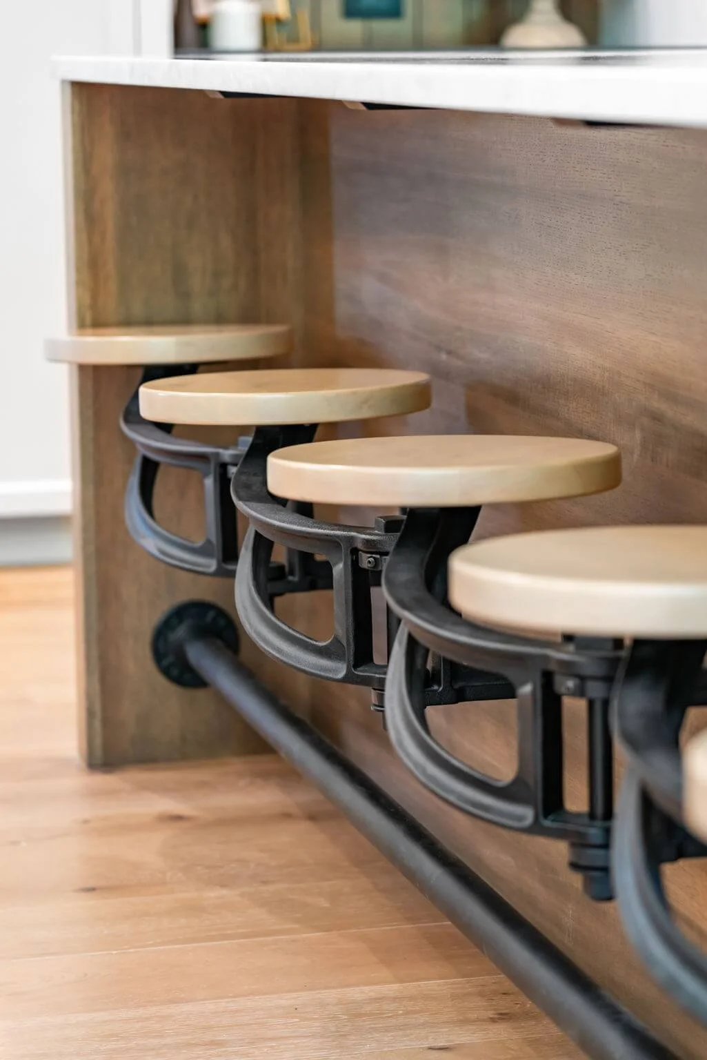 Three height-adjustable bar stools with light-colored wooden seats and black metal frames, attached to a bar-height counter in a modern kitchen or dining area.