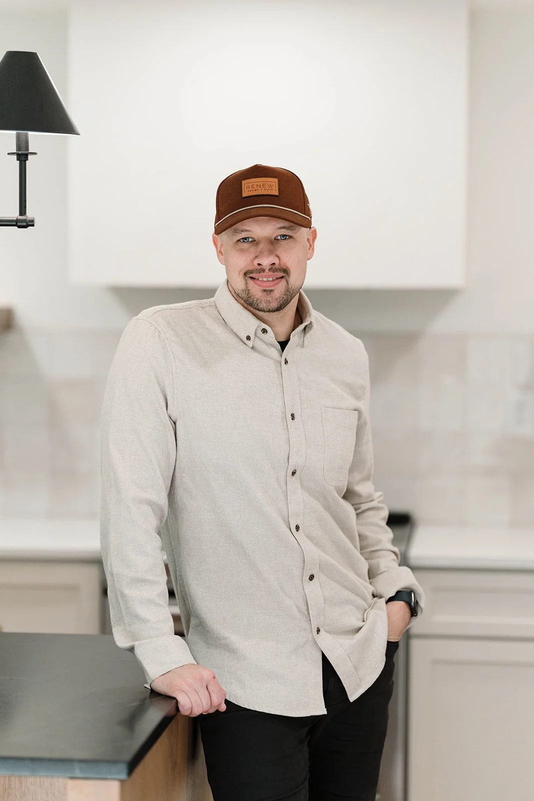 President of Renew Design + Build, Josh Holmgren, standing in a modern kitchen with white cabinets and a black countertop.
