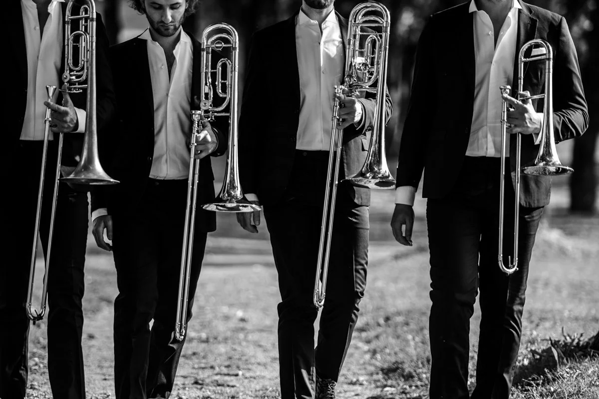 Quattro uomini in abito elegante che camminano con tuba in mano, in un'immagine in bianco e nero.