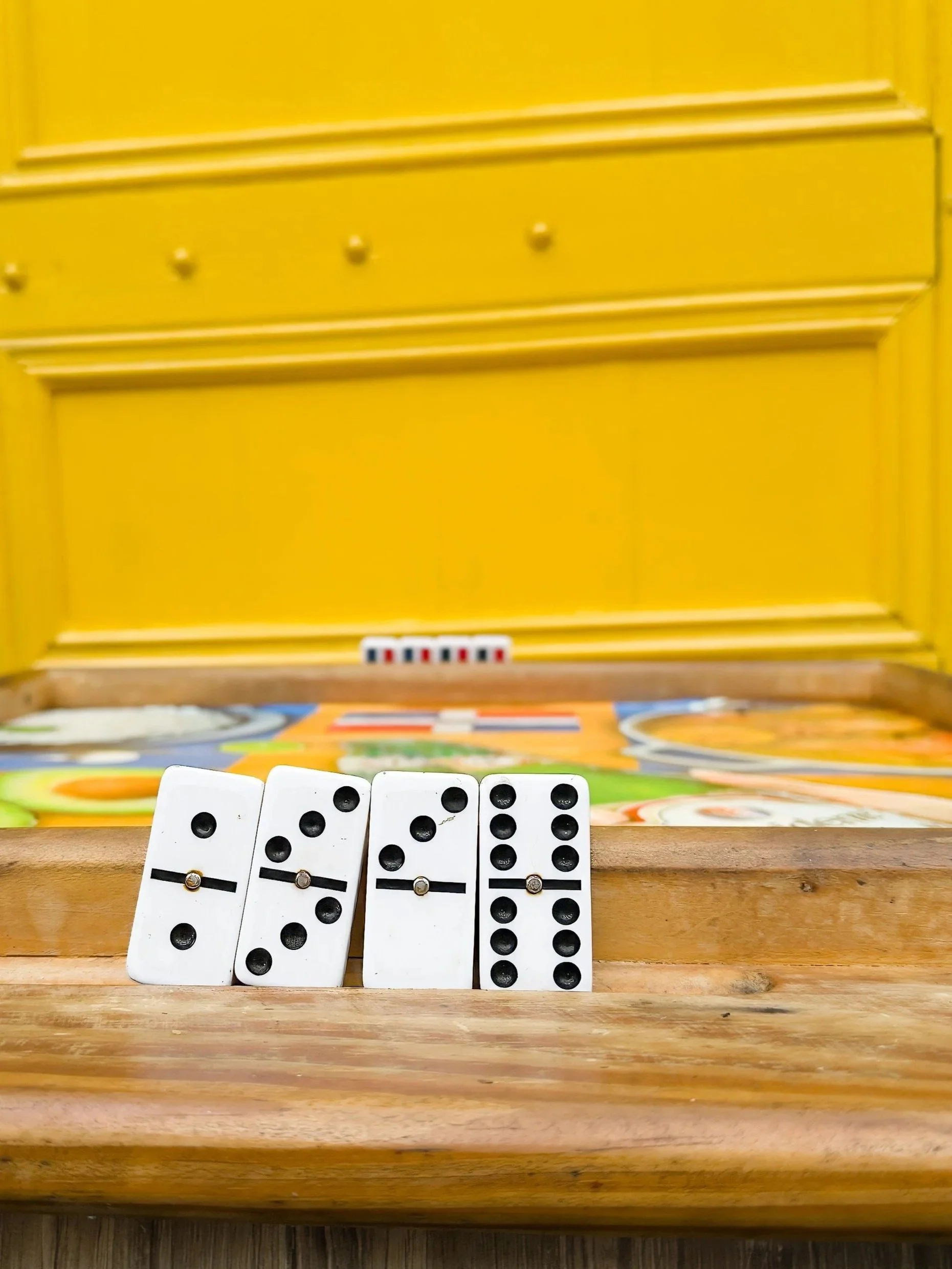 Close-up of four domino tiles standing upright on a wooden game board, with a yellow wall in the background.