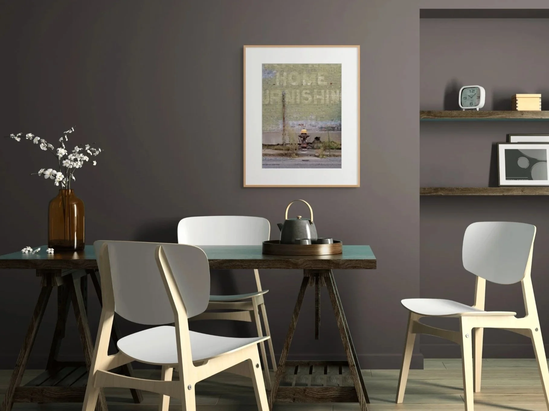 A modern dining room with a dark wall, white chairs around a wooden table, a brown vase with white flowers on the table, and a framed picture on the wall. There is a shelf with a clock, books, and framed artwork.