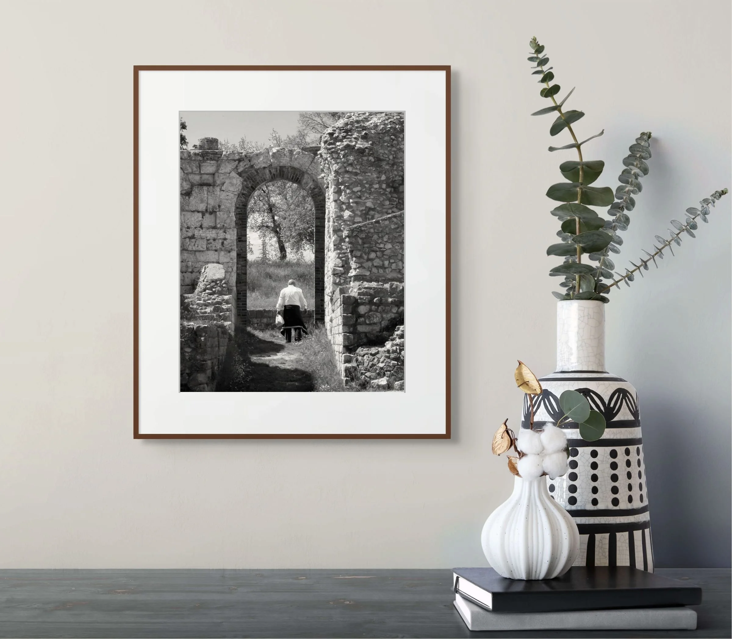 An older man, in a white shirt, walks by himself through an arch of a amphitheater ruin in Italy.